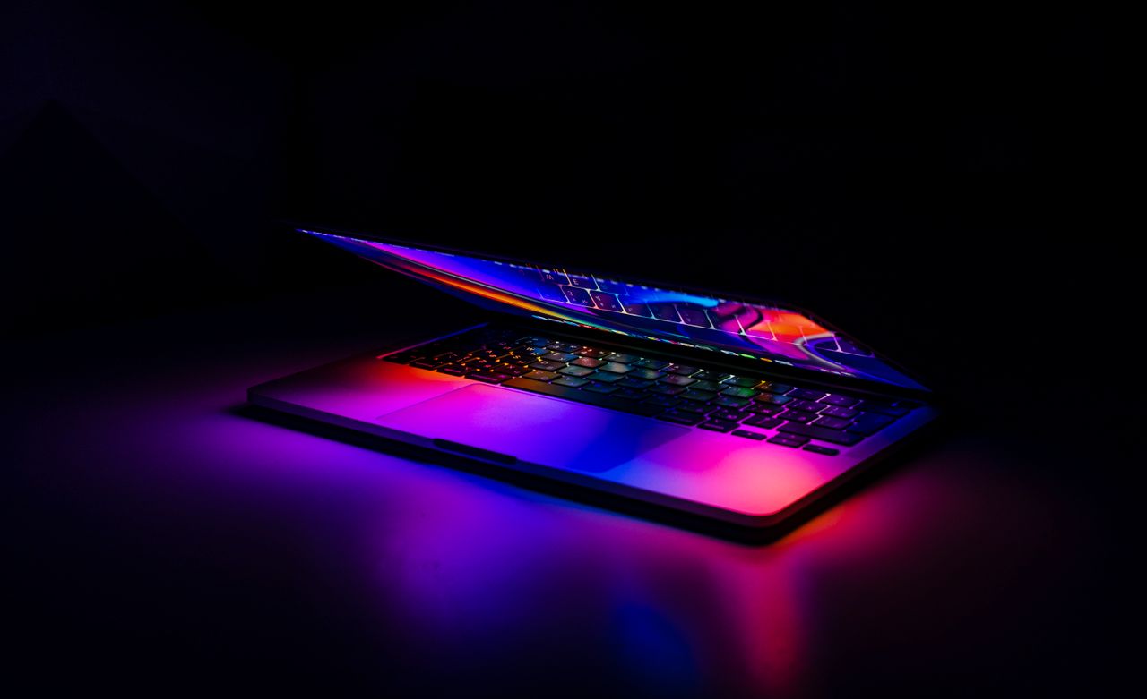 A partially closed MacBook with vibrant, colorful light reflections on a dark background.