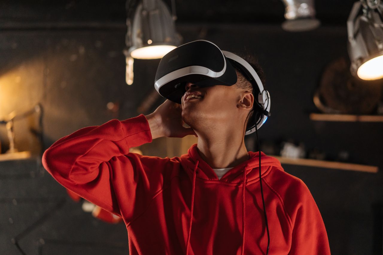 A young man wearing a red hoodie explores virtual reality indoors with a VR headset.